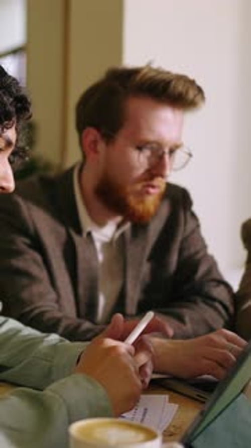 Young Professionals Collaborating in Cozy Cafe Workspace Focused on Digital Tablets Notes and Coffee