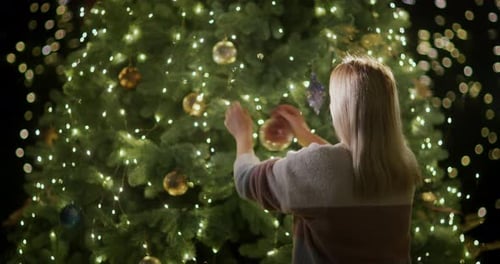 Woman Decorates Christmas Tree With Lights and Ornaments