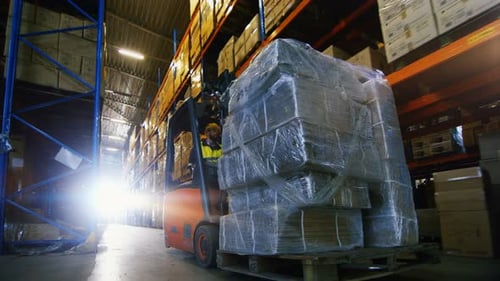 Professional Driver Operates Forklift Truck with Cargo in Big Warehouse.