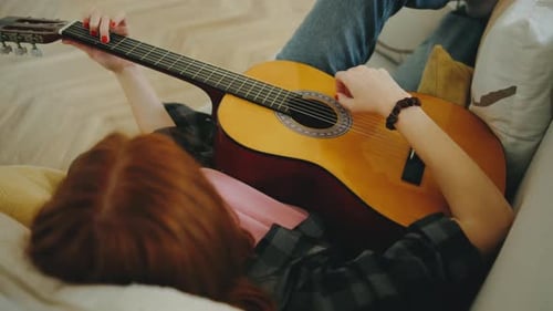Woman Lying on Couch Playing Acoustic Guitar