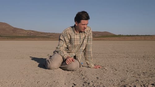 A Sad Young Man Sits on the Lifeless Land That Remains From a Driedup Lake Global Warming Changing