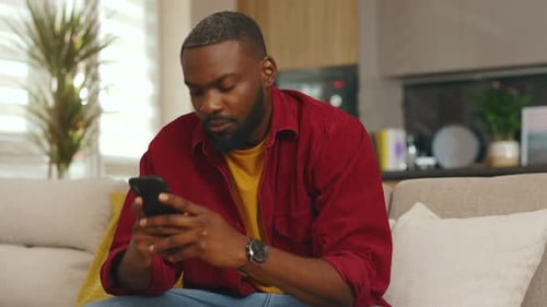 Close Up of Young African American Man Use Phone Sit on Sofa in Home Communication in Social Media