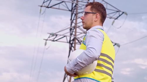 A designer inspects a high voltage tower. An engineer in a hard hat servicing a power transmission p