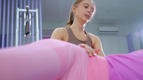 Gym Instructor Monitors Lady in Pink During Workout in WellLit Gym