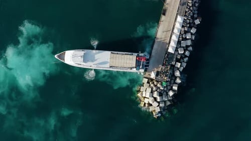 Top Down Aerial Drone Shot of Passenger Ferry Arriving at Vibrant Coastal Harbor with Emerald
