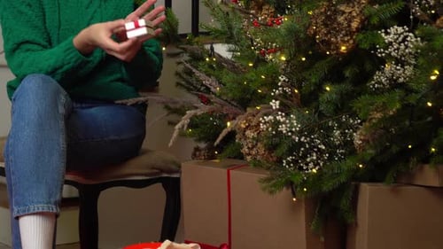 Woman Happily Opens Gift by Christmas Tree