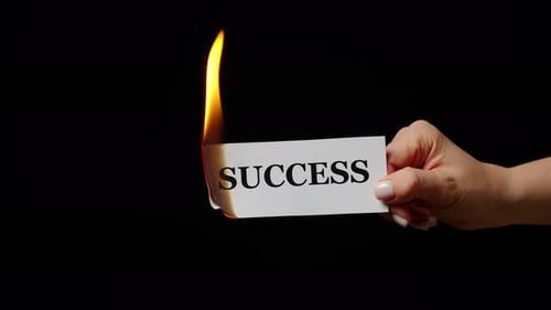 Hand Holding Flaming Paper with Word Success in Studio