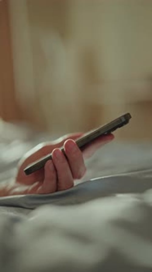 Vertical Side View Shot of Unrecognizable Man Relaxing Lying Alone in Bed Using Smartphone to Browse