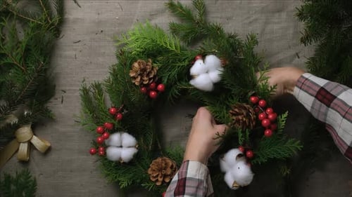 Hands Crafting Christmas Wreath with Berries and Pine Cones
