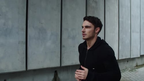 Focused young man training run outdoors on urban street in slow motion