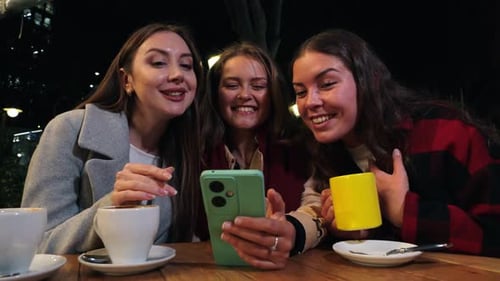Friends Video Chatting on Smartphone at Night Cafe