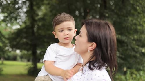 Mother Holds Child in a Green Urban Park