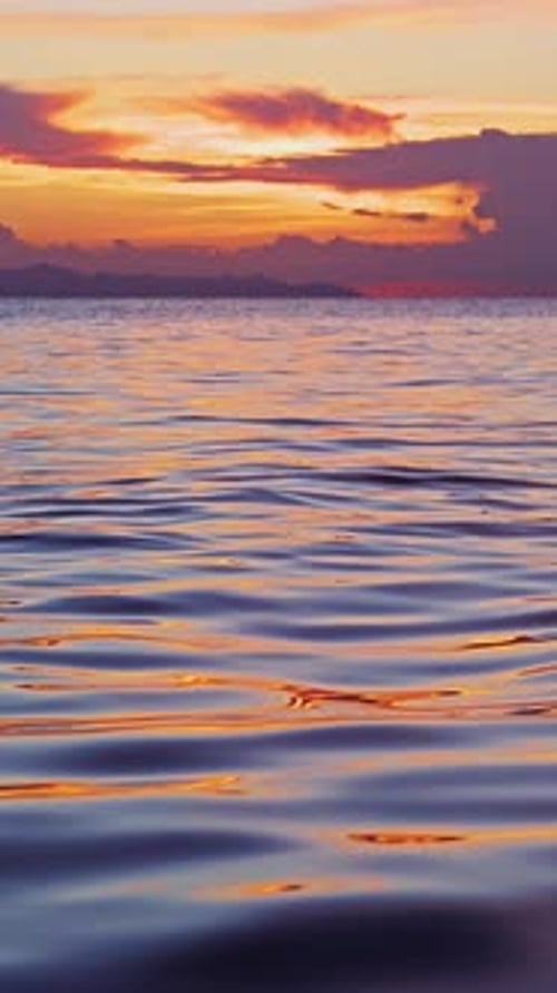 Vertical video. Low Angle View Of Calm Ocean Waves Reflecting Vibrant Sunset Colors In Slow Motion,