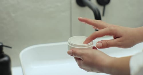 Woman Applying Cream to Hand in Bathroom