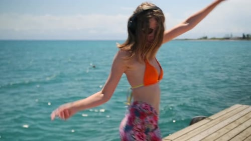 Young dancing woman in bikini enjoying her vacation on pier seashore next to sea, freedom