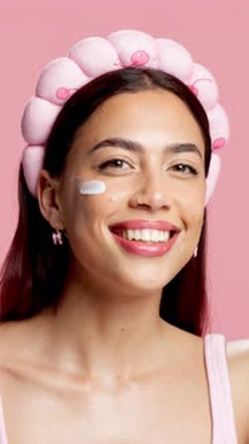 Woman, skincare cream and face in studio with headband, happy and pride on pink background