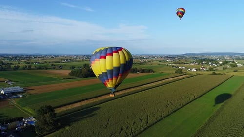 Aerial view of a hot air balloons floating thru the farms during a festival on a sunny summer day in