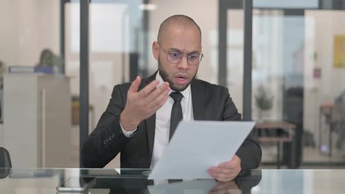 Man Looks at Paperwork with Frustration in Office