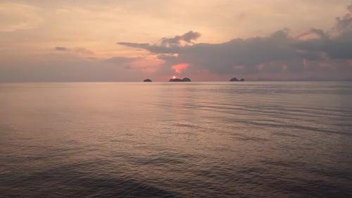 Drone's Flight Along Serene Sea Towards Vibrant Orange Sunset Against Mountains Captures Rest This