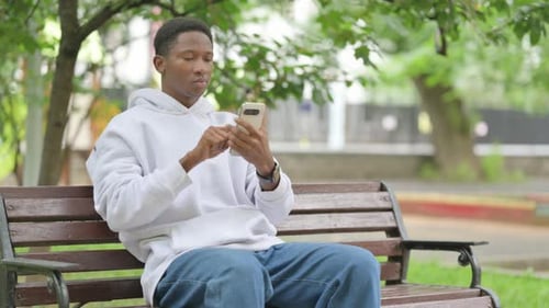 Young Adult Using Smartphone on a Park Bench