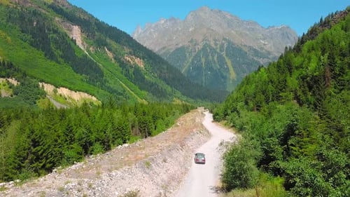 Car moves along dusty road among mountains in gorges.