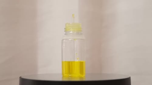 Pequeña botella llena de líquido amarillo que gira sobre fondo blanco