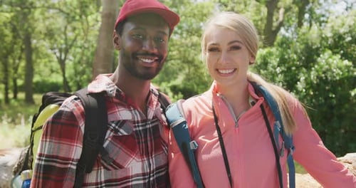 Portrait of happy diverse couple with backpacks embracing in park, slow motion