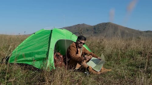 Man Camping and Reading Map in Grassy Field