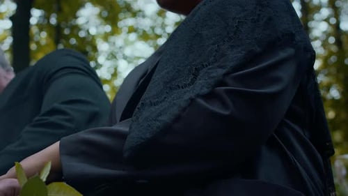 Woman with Roses on Her Lap Holding Hand of Husband during Visit in Cemetery