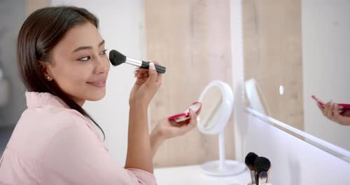 Woman Applies Makeup With Brush in Bathroom