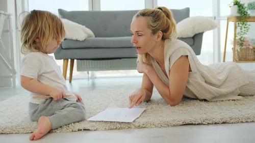 Mother Watching Young Child Drawing on Carpet