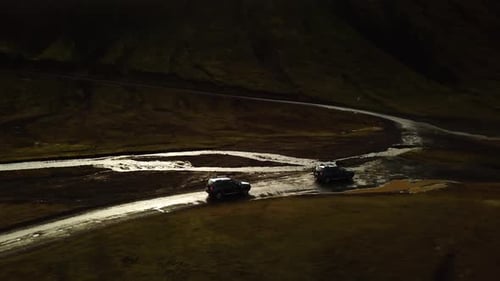 Luftaufnahme von Autos mit Allradantrieb, die auf einer unbefestigten Straße fahren und einen schlammigen Fluss überqueren