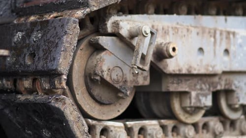 Close-up of asphalt tracked paver tracks slowly moving on fresh new road at construction site