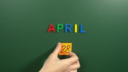 Hand sticking a sticker 28 April calendar day on school board. 28 date of April. Twenty eighth day