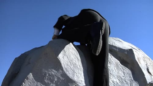 Businessman climbing rock face reaching for success under a blue sky