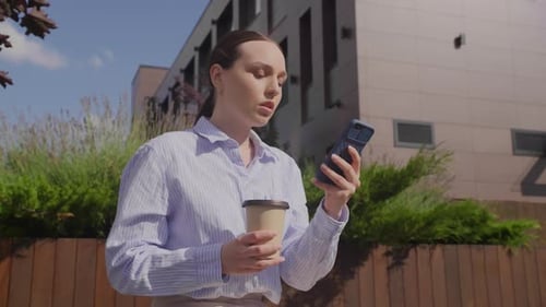 Young Woman Using Smartphone Holding Coffee Outdoors