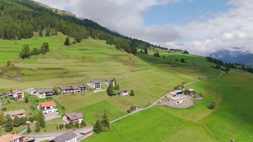 Aerial flight uphill green mountains with houses and homes on alp mountain In summer. Wide shot.