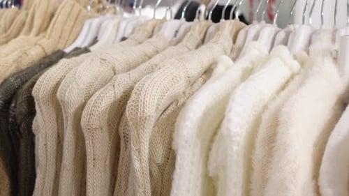 A Collection of Neutral Colored Knitted Sweaters Hanging on Display Rack in a Fashion Store
