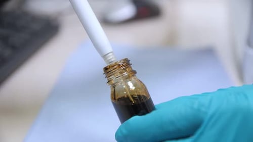 Empleado saca petróleo crudo de una botella con una jeringa en el laboratorio