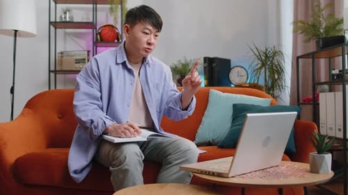 Man Video Conferencing and Taking Notes at Home