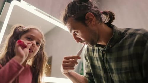 Father and Daughter Brushing Teeth Together in Bathroom