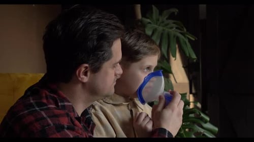 Adult Helping Child Using Nebulizer Mask Indoors