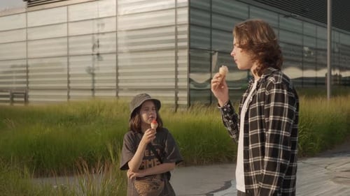 Two boys are standing, talking and eating ice cream in a city park in the summer