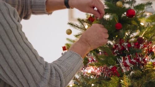 Man Decorating Christmas Tree Wearing Santa Hat Indoors