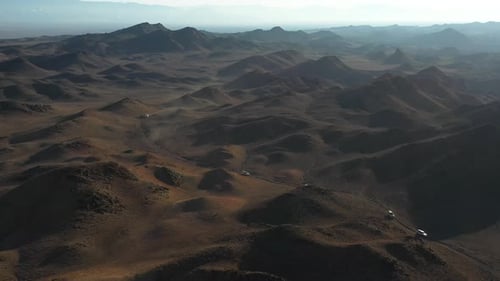 Rotating cinematic drone shot of a caravanning fleet of cars through Charyn Canyon, Kazakhstan