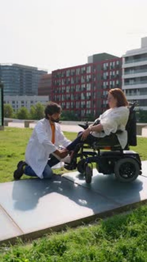 Doctor Adjusting Disabled Woman's Footrest in Urban Park