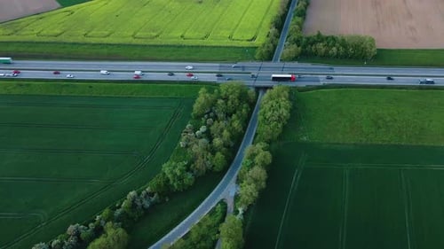 Aerial View of Highway Traffic Through Through Rural Landscape with Green Farmland