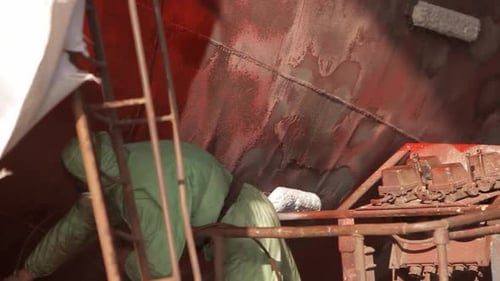Trabalhador em equipamento de proteção pinta casco em estaleiro Manutenção marítima industrial Renovação de navios
