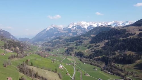Drone flight through a green swiss valley in the alps with snow and blue sky