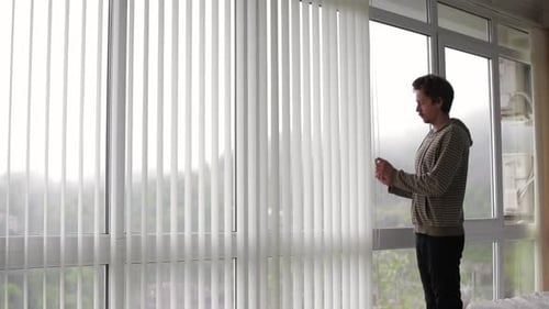 Man Adjusting Vertical Window Blinds Filtering Daylight Streaming Through Contemporary Apartment